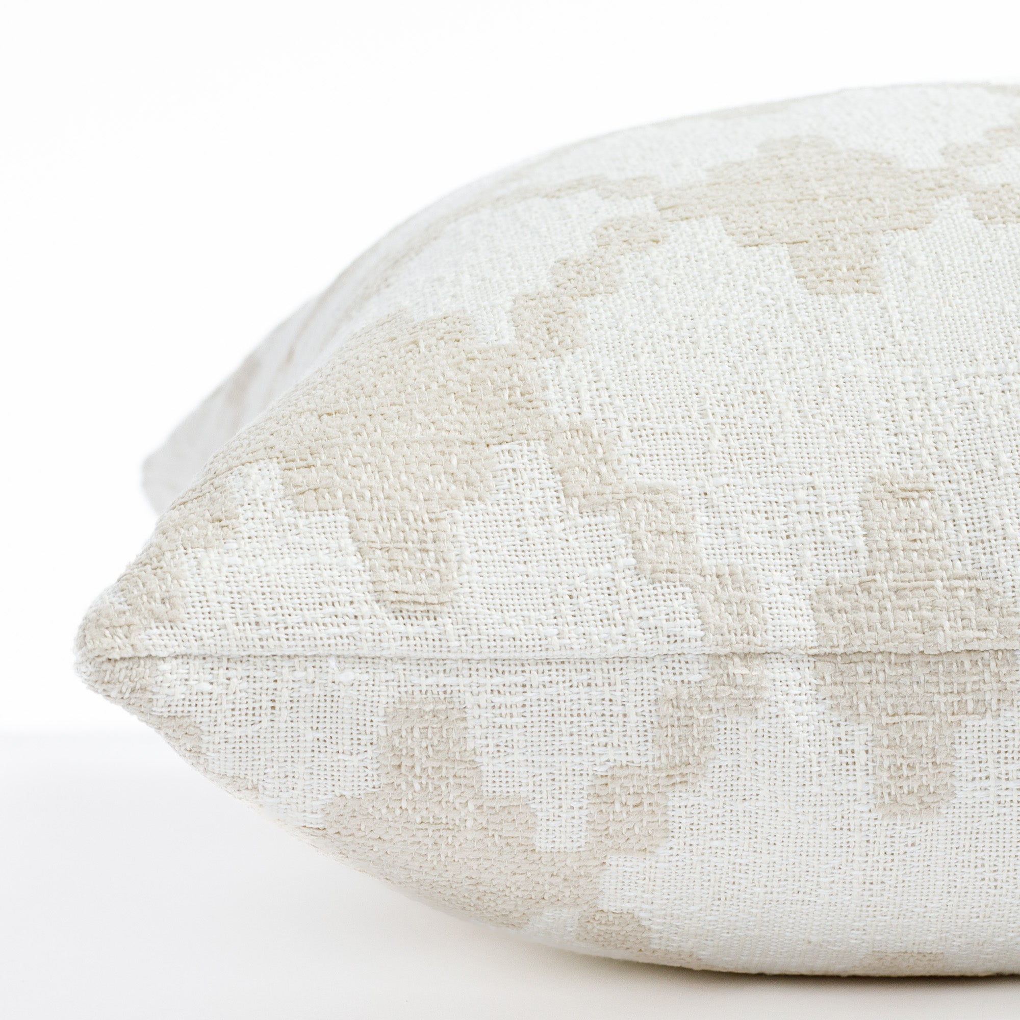 a white and beige diamond trellis patterned pillow: close up side view