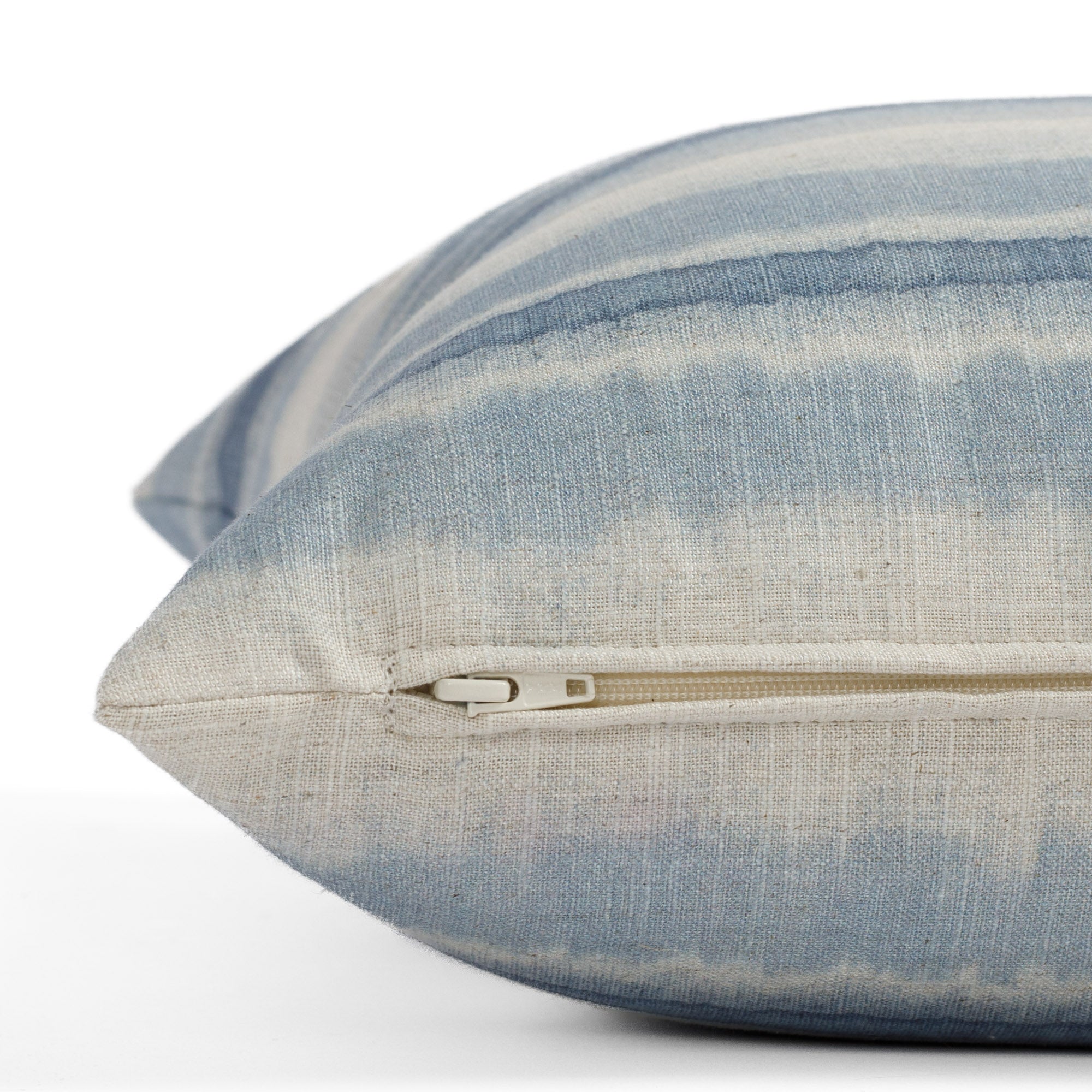 A denim blue and beige pillow with faded stripes: close up zipper view.